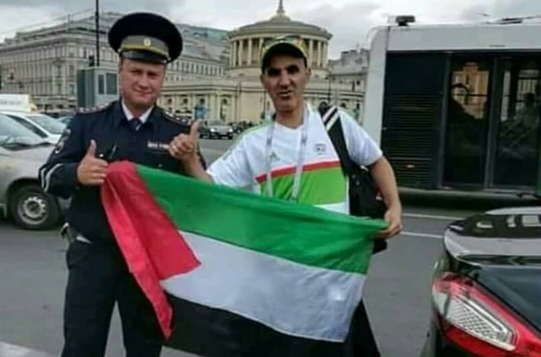مشجّع جزائري يرفع علم فلسطين إلى جانب شرطي روسي مشجّع جزائري يرفع علم فلسطين إلى جانب شرطي روسي
