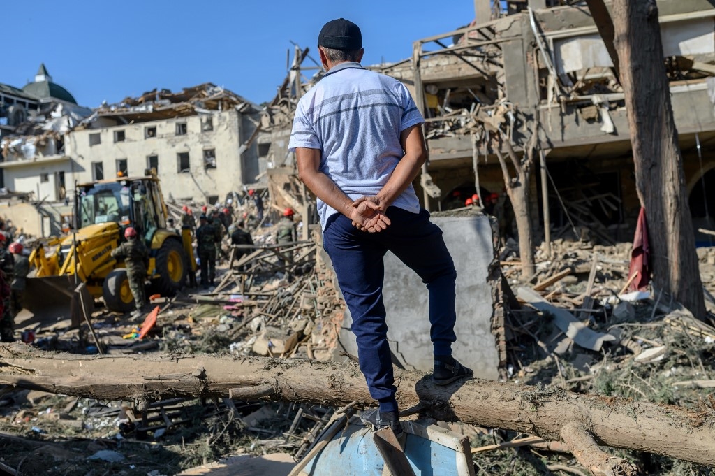 رجل يراقب رجال الإنقاذ وهم يبحثون عن ناجين في موقع انفجار في ناغورنو كاراباخ خلال الاشتباكات - 11 أكتوبر 2020 (أ.ف.ب)