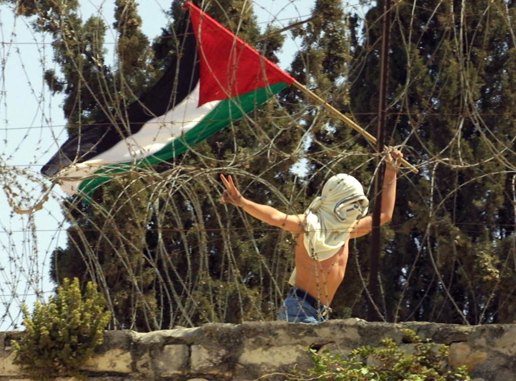 شاب يحمل العلم الفلسطيني ويرفع علامة النصر قرب المسجد الأقصى خلال اشتباكات مع الاحتلال عام 2001 (أ.ف.ب)