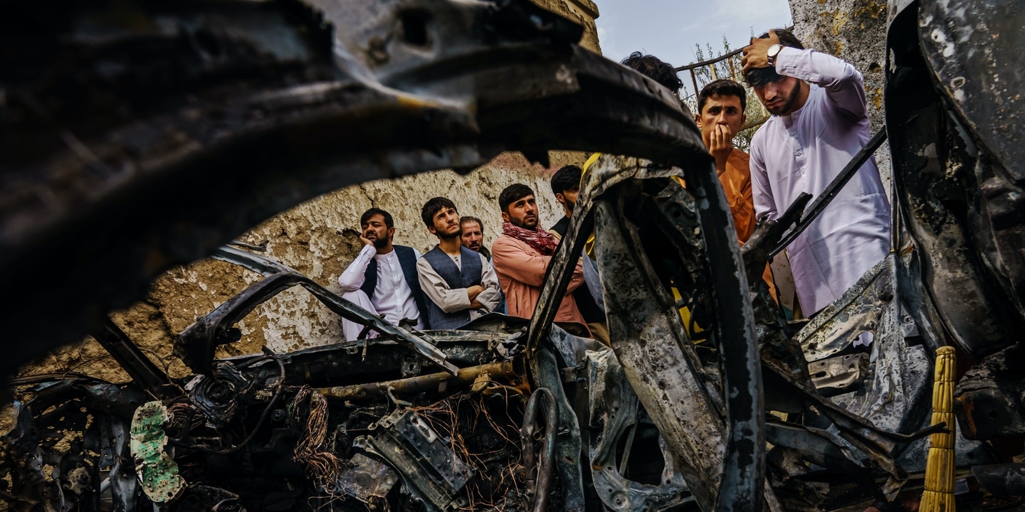 Relatives of the Ahmadi family gather around the incinerated husk of a vehicle targeted and hit by a US drone strike that left 10 dead, Kabul, Aug 30, 2021 | Getty